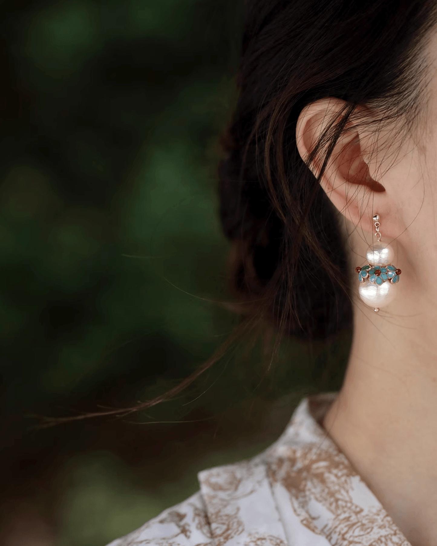 Side profile of earrings showing shimmer of pearls and enamel shine under natural light