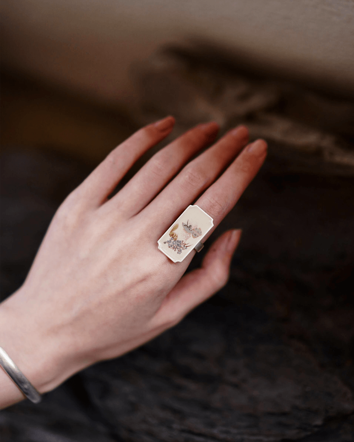 Close-up of hand-painted Chinese lacquer ring with squirrel and grape motif in silver frame