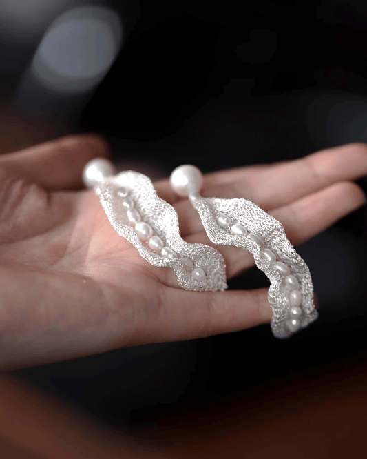 Close-up of delicate silver mesh threads forming pea pod shape with nestled luminous pearls