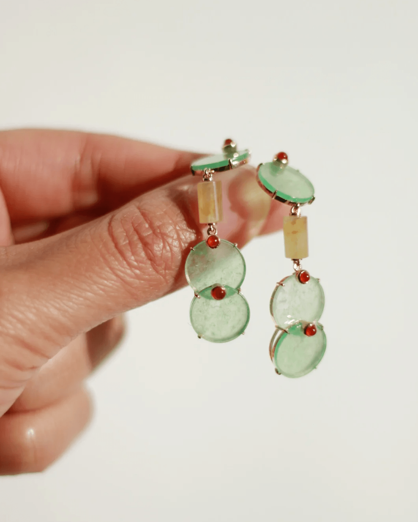 Close-up of earrings in motion, showing light catching the jade’s glow and carnelian’s spark