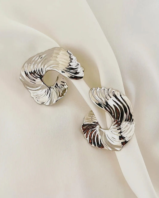 Close-up of silver earrings showing hammered metal folds mimicking silk ripples in dawn light