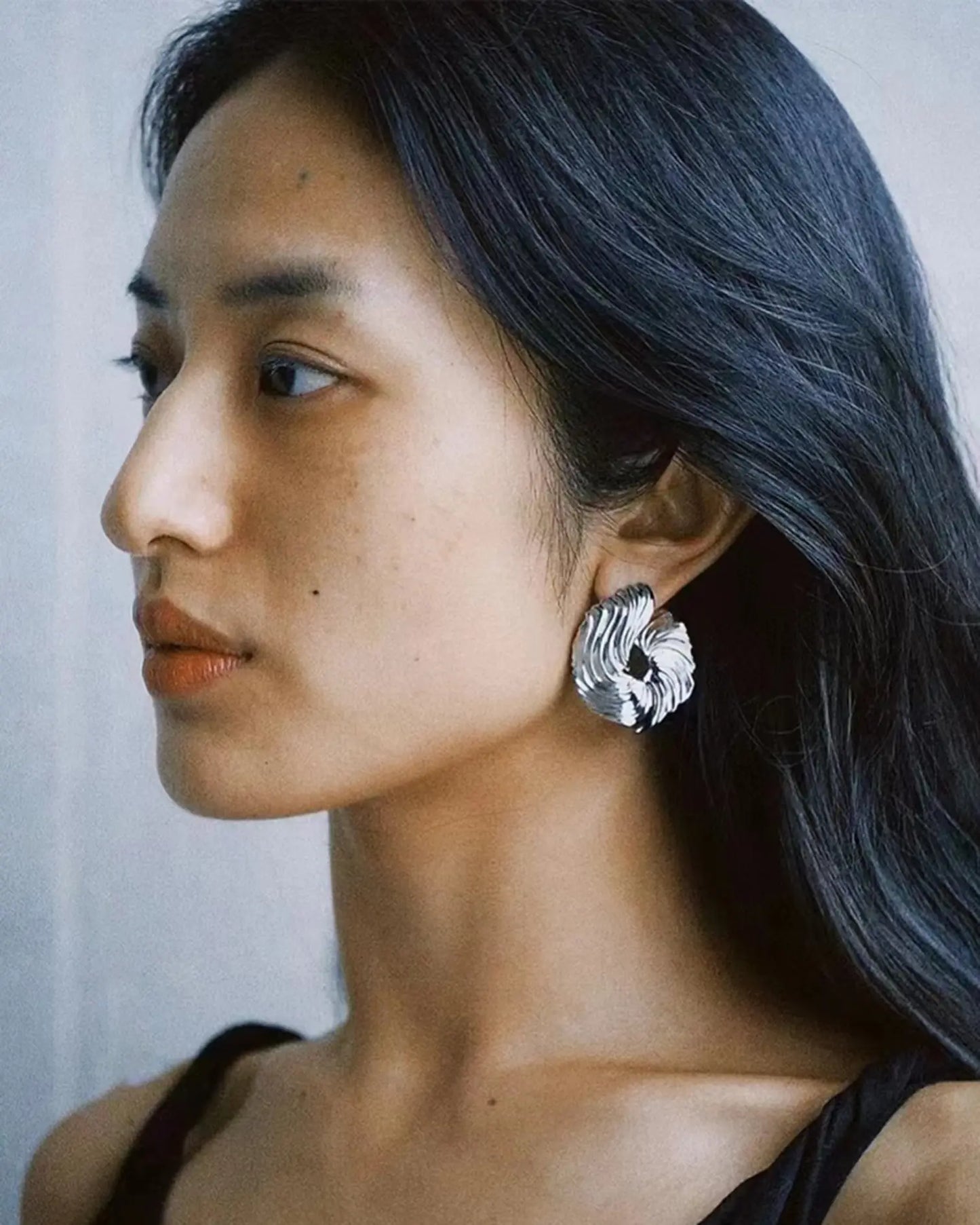 Side profile of earrings catching natural light, emphasizing sculptural form and soft metallic shine