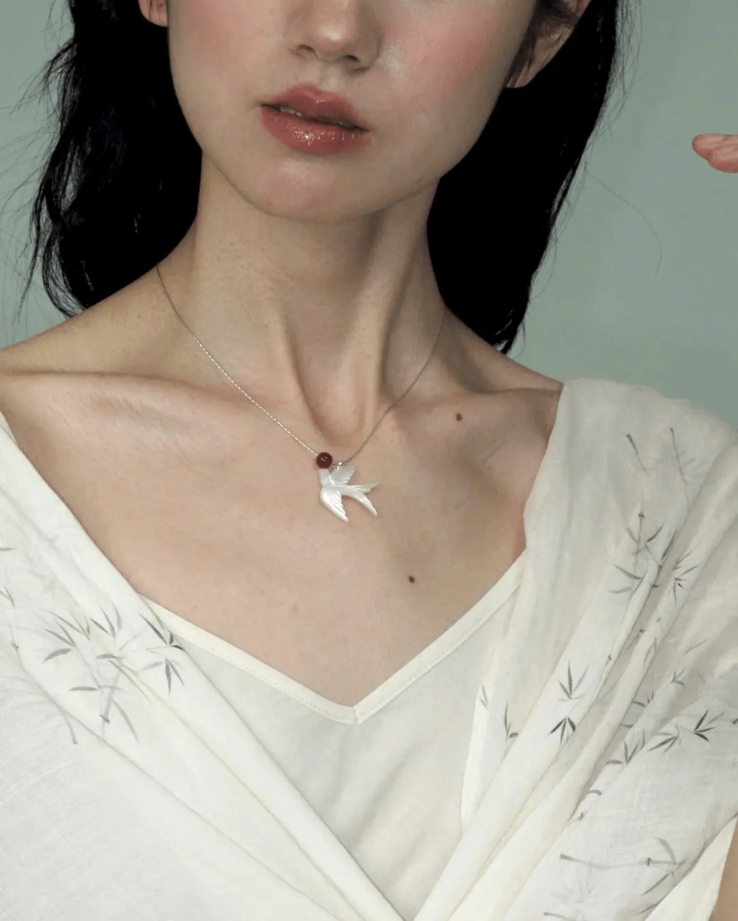 Model wearing phoenix necklace with silk V-neck blouse, showcasing elegant yin-yang energy in motion
