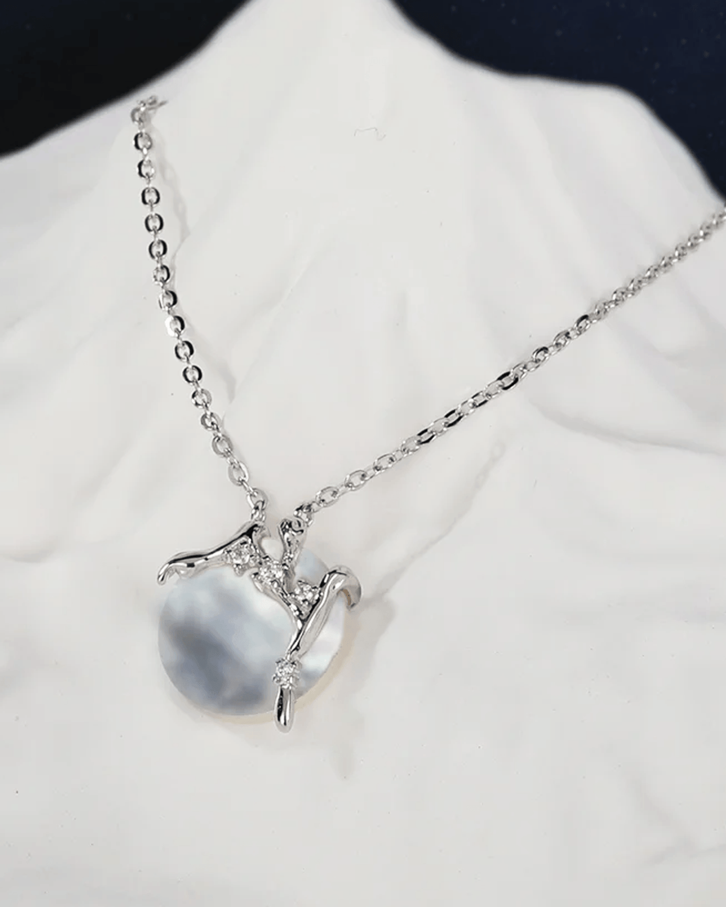 Flat lay of mother-of-pearl crescent moon necklace with rhodium-plated silver chain featuring hand-etched willow bark texture