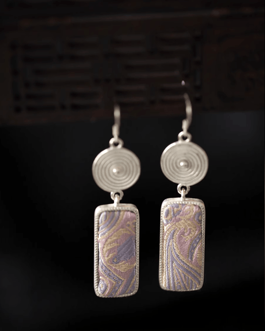 Flat lay of Fluid Mirage earrings featuring 0.5-inch wide Song brocade silk tassels and pure silver ear hooks