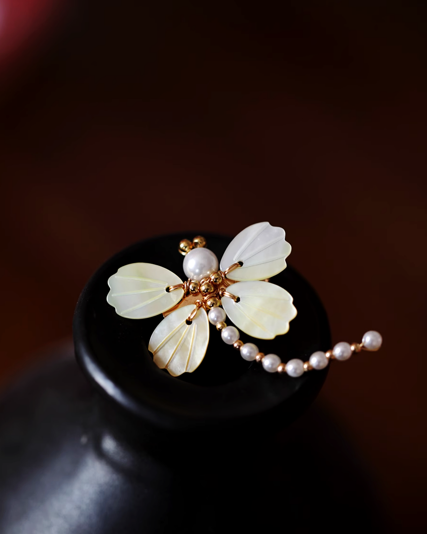 Flat lay of dragonfly brooch with iridescent mother-of-pearl wings and hand-strung seed pearl body, inspired by lotus pond poetry