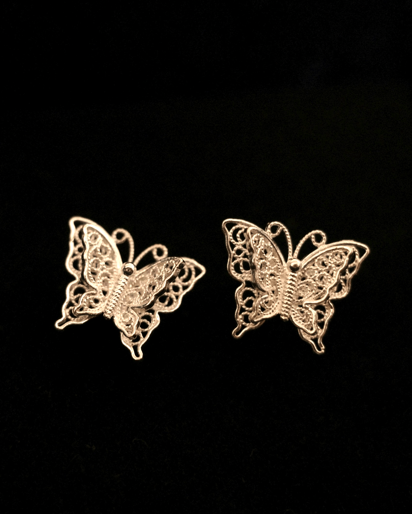 Close-up of handmade filigree earrings with 0.2mm silver wires forming butterfly wings