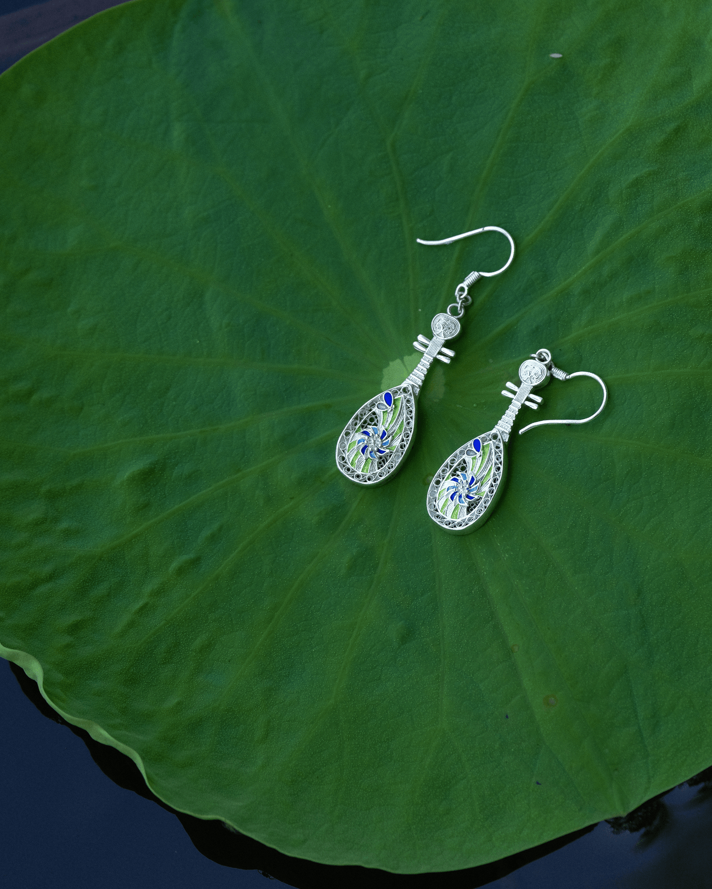 Sterling silver filigree pipa earrings with cloisonné enamel resting on a lotus leaf — handcrafted Chinese cultural jewelry inspired by Dunhuang.