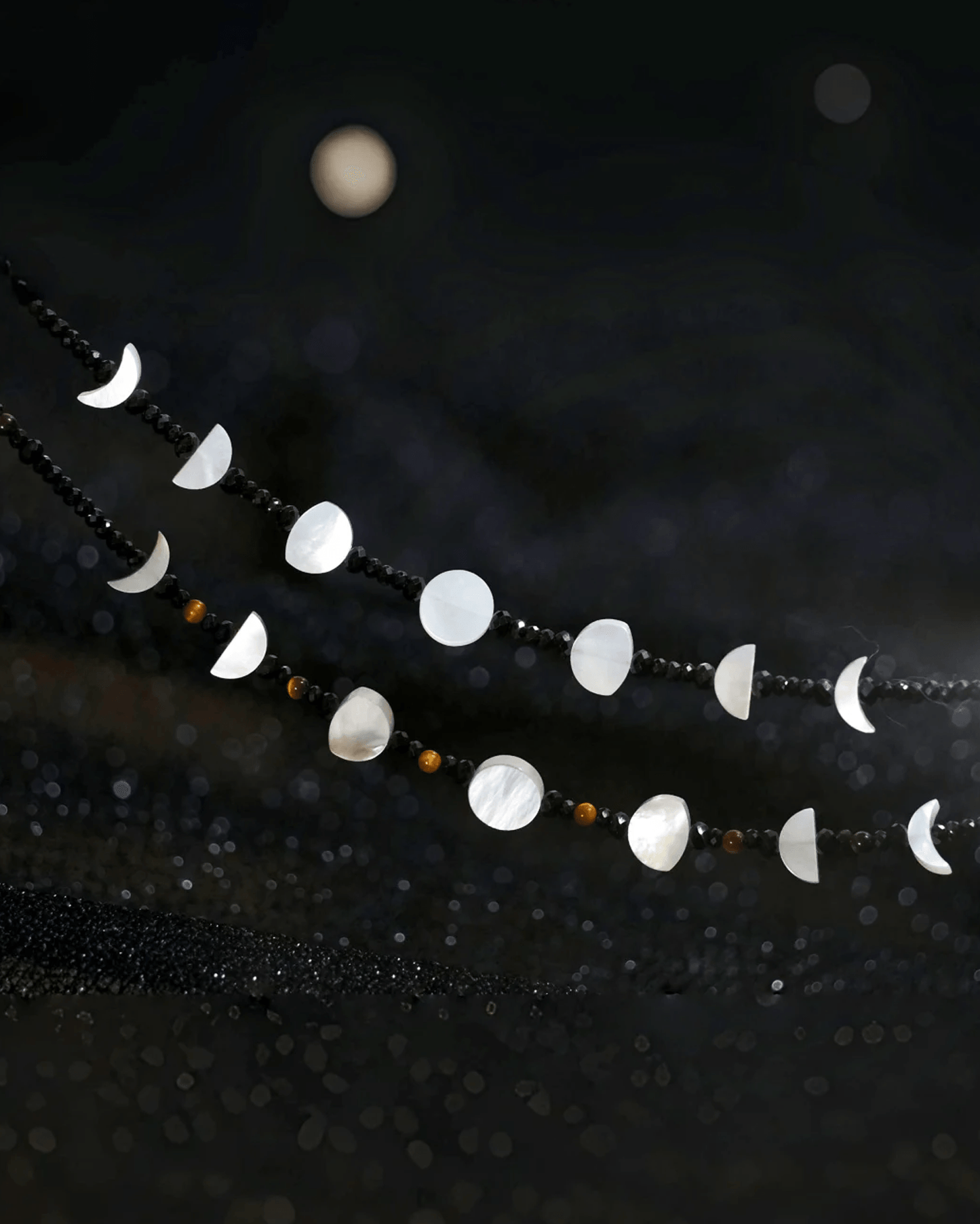 Flat lay of tiger’s eye lunar necklace with rotating moon phase charms, inspired by Eastern yin-yang and cosmic rhythm
