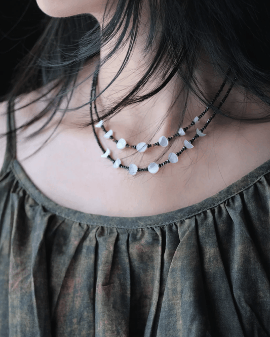 Side view of necklace worn solo with deep neckline, lunar charms reflecting ambient light for mystical effect