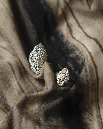 Sterling silver ring placed on embroidered cloth with Yi ethnic symbols and aged wood background, honoring craft roots