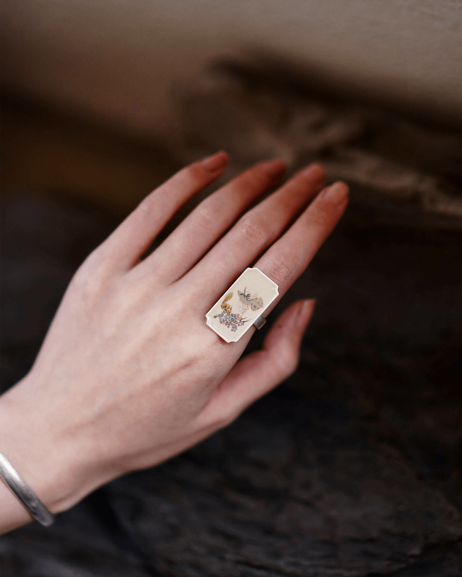 Close-up of hand-painted Chinese lacquer ring with squirrel and grape motif in silver frame