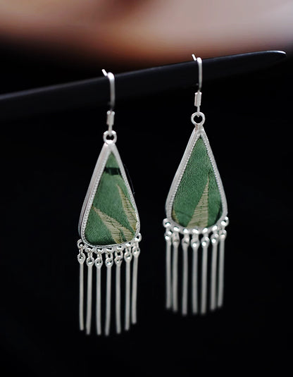 Handcrafted Chinese textile jewelry featuring jade-toned song brocade and silver tassels. Featherlight triangle earrings blending ancient silk art.
