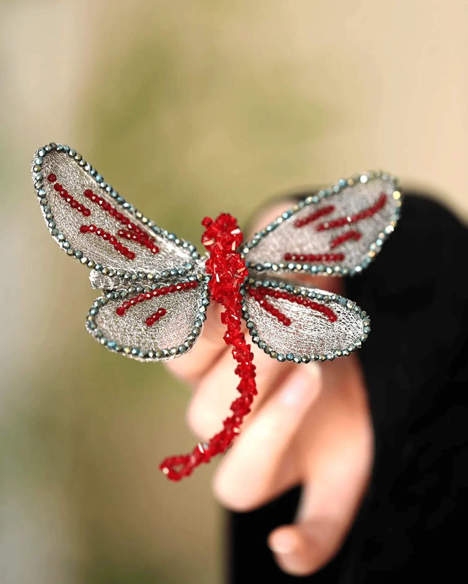 Flat lay of hand-embroidered dragonfly hair clip with iridescent silk thread and secure grip backing