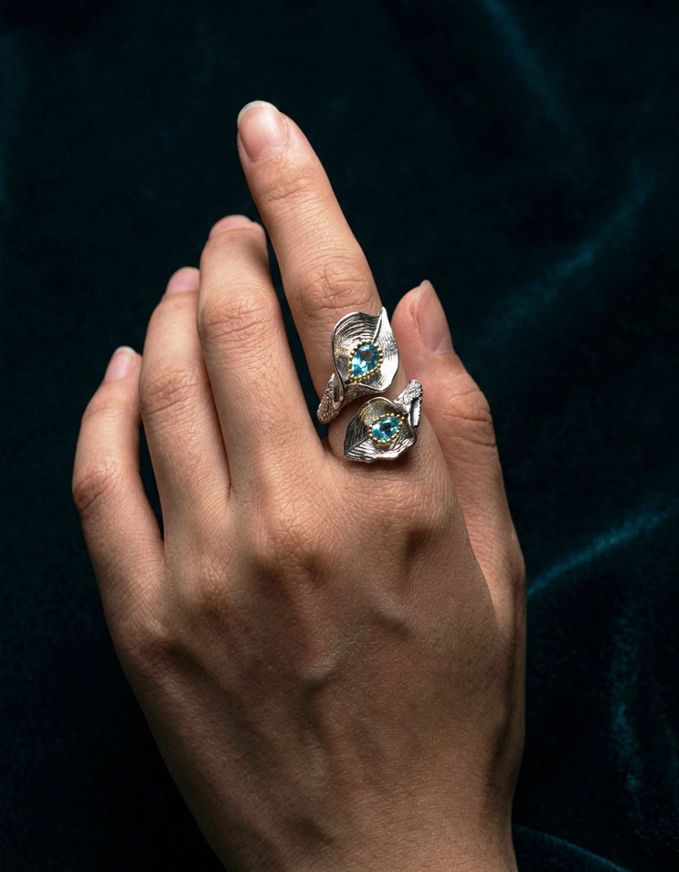 Side view of blue topaz ring on finger, reflecting light with elegant shimmer against minimalist outfit