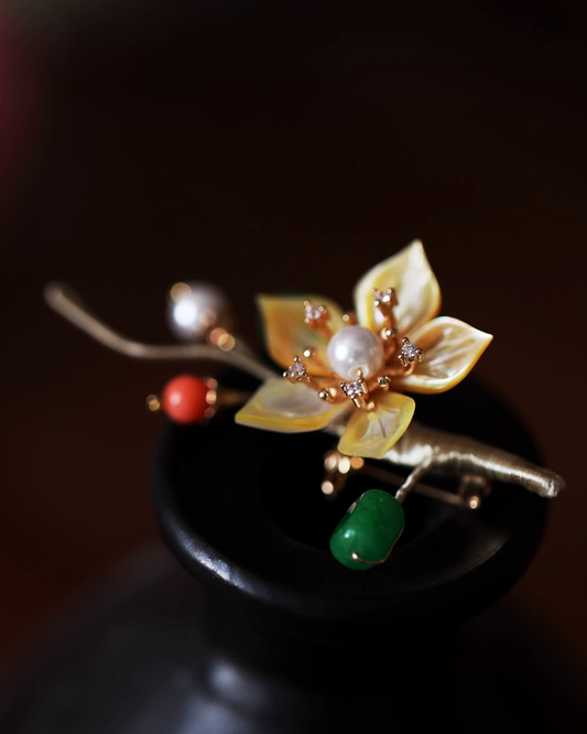 Flat lay of mother-of-pearl plum blossom brooch with hand-carved translucent petals and pearl stamens, inspired by Chinese poetry