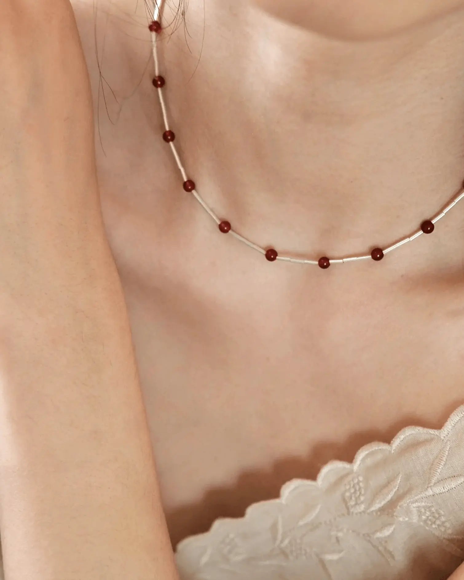 Model wearing red agate charm necklace with white blouse, evoking modern luck and heritage symbolism