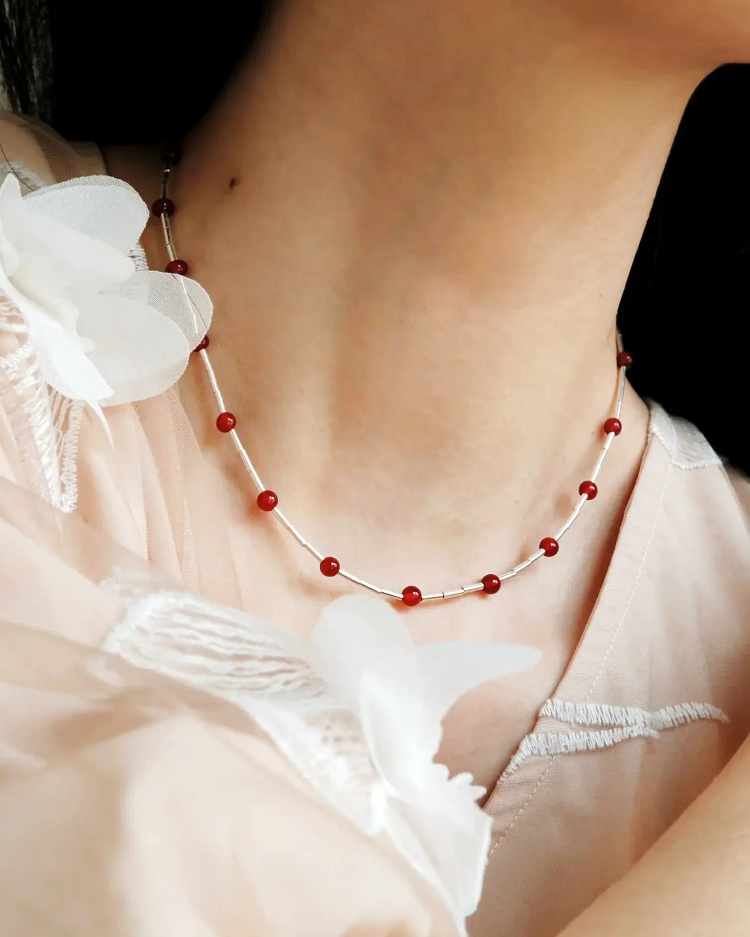 Side view of necklace styled with deep V-neck top, highlighting red gemstone glow and silver movement