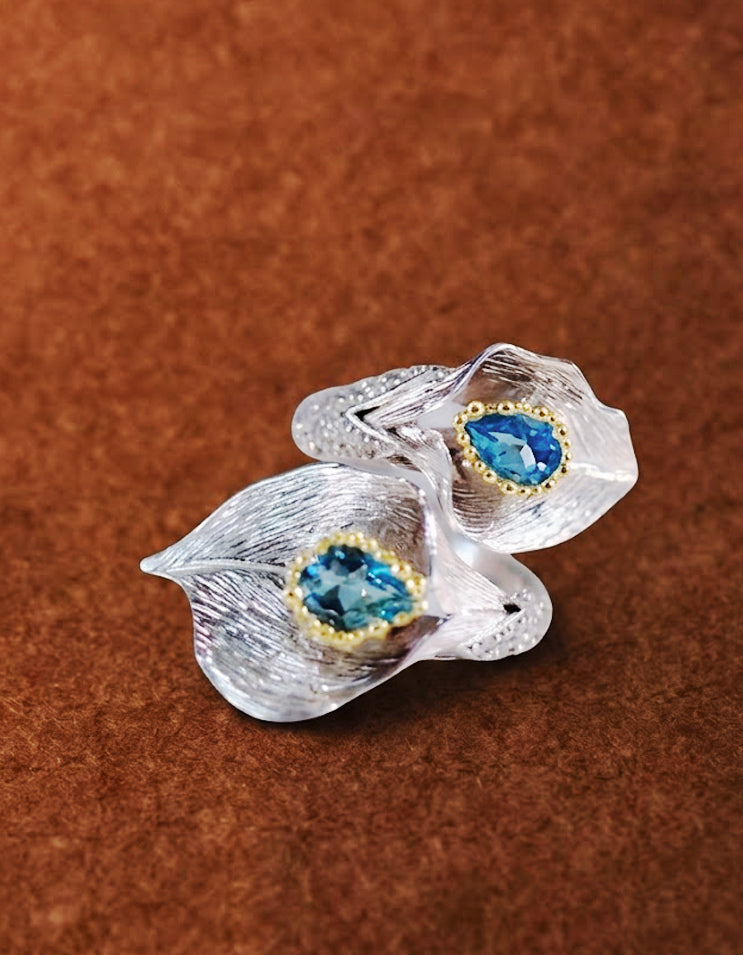 Close-up of blue topaz gemstone reflecting moonlit lake hues, embraced by two calla lily petals
