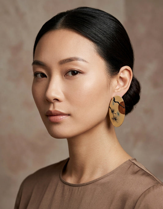 A woman wearing a miniature classical landscape Chinese lacquer wood earrings feature hand-painted pine & sunset motifs on burnished bronze lacquer. Da Qi art.