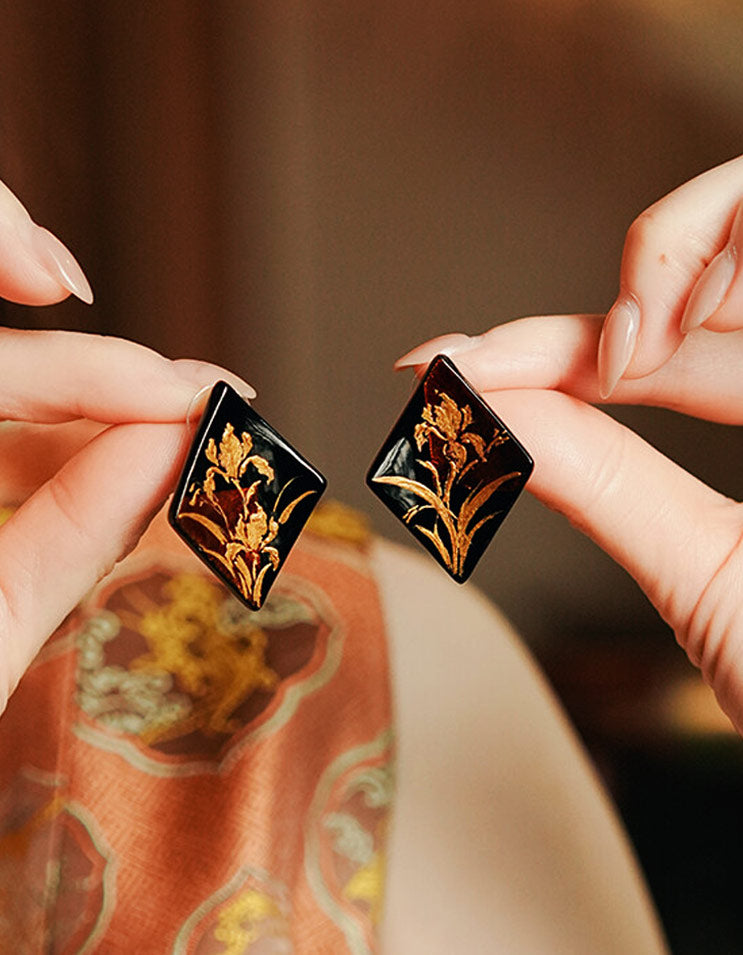 Close-up of diamond-shaped lacquer earrings featuring hand-painted gold iris flowers.