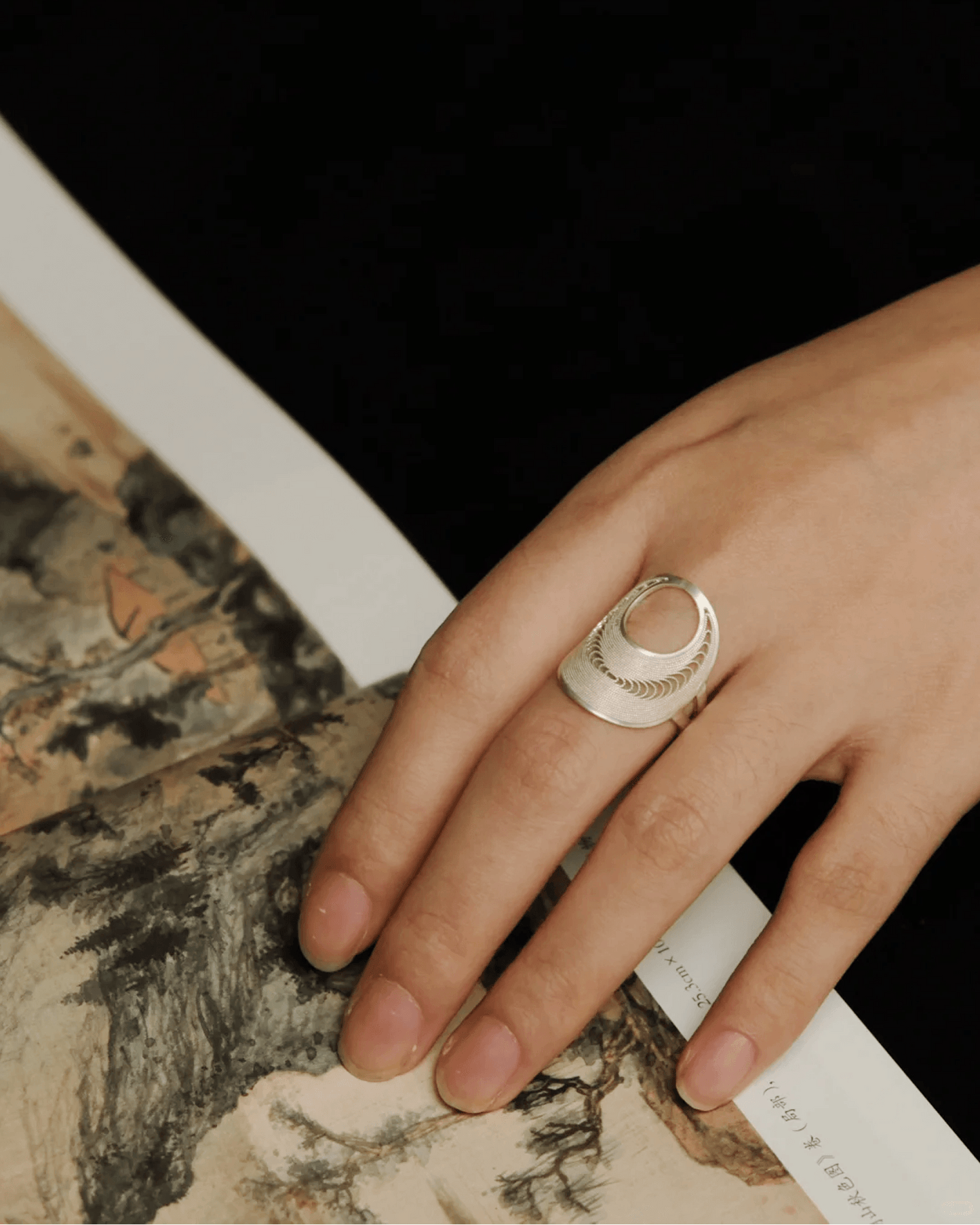 silver filigree ring on hand over Chinese ink painting – heritage jewelry style