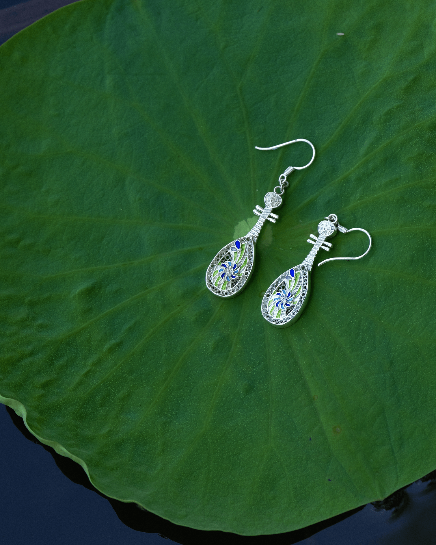 Sterling silver filigree pipa earrings with cloisonné enamel resting on a lotus leaf — handcrafted Chinese cultural jewelry inspired by Dunhuang.