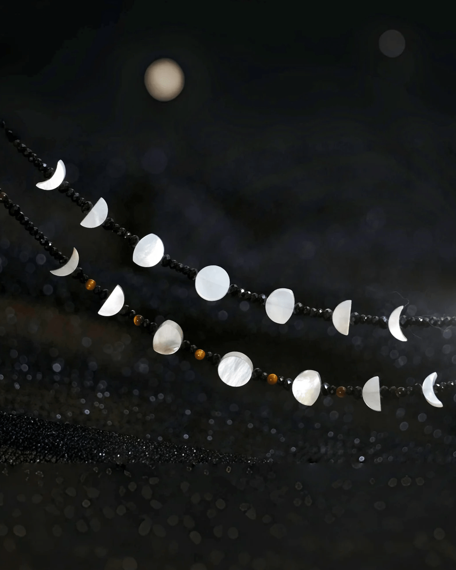 Flat lay of tiger’s eye lunar necklace with rotating moon phase charms, inspired by Eastern yin-yang and cosmic rhythm