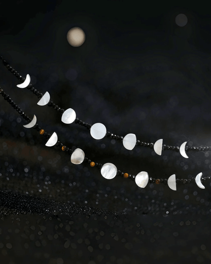 Flat lay of tiger’s eye lunar necklace with rotating moon phase charms, inspired by Eastern yin-yang and cosmic rhythm